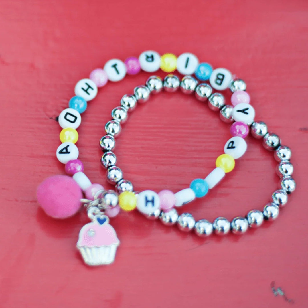 Colorful beaded bracelet with letter beads spelling Happy Birthday, a pink pom-pom and a pink frosted cupcake charm with the silver beaded bracelet included in the set from Great Pretenders