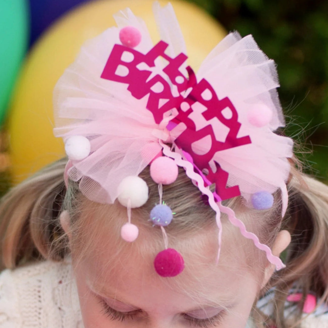 Young girl blowing out candles on a birthday cake with the Happy Birthday headband on her head