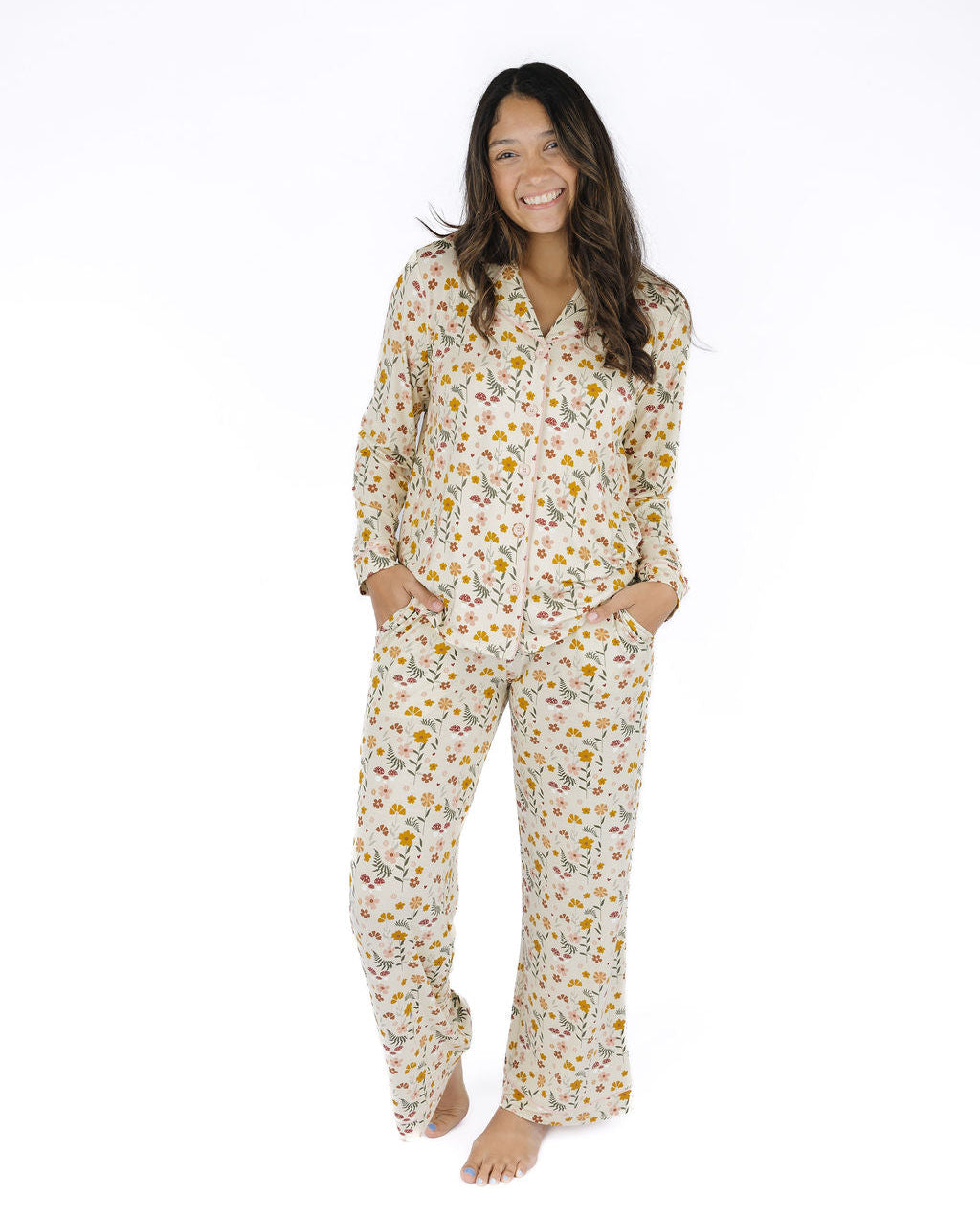 A woman modeling a matching long-sleeve pajama set with a white base and a small yellow, orange, and green floral print, standing against a plain white background.