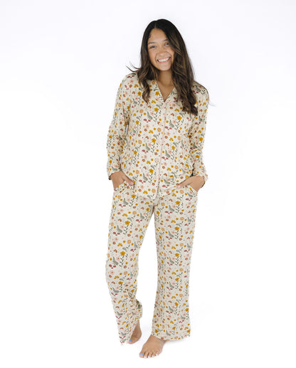A woman modeling a matching long-sleeve pajama set with a white base and a small yellow, orange, and green floral print, standing against a plain white background.
