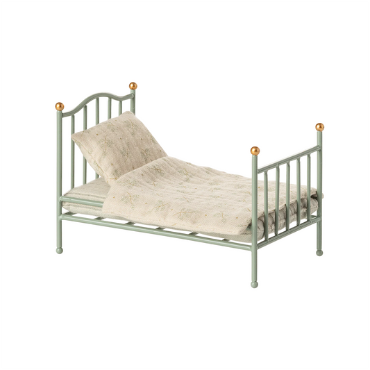Green metal bed with beige bedding on a white background