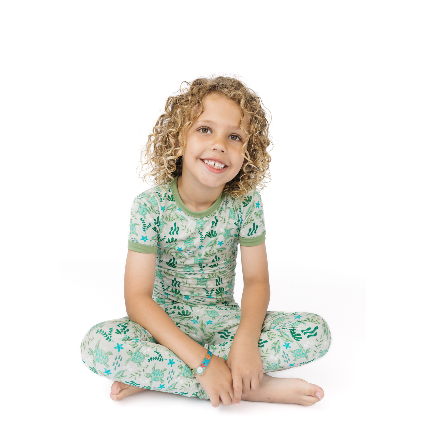 Child wearing a green and white pajama set with a sea turtle pattern on a white background