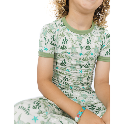Child wearing a green and white patterned outfit with sea turtle design on a white background