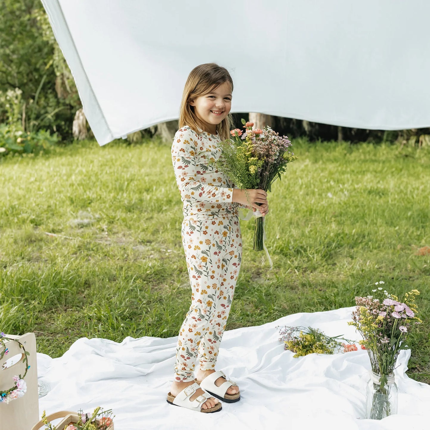 girl wearing cream pj set with floral print on greenery background.