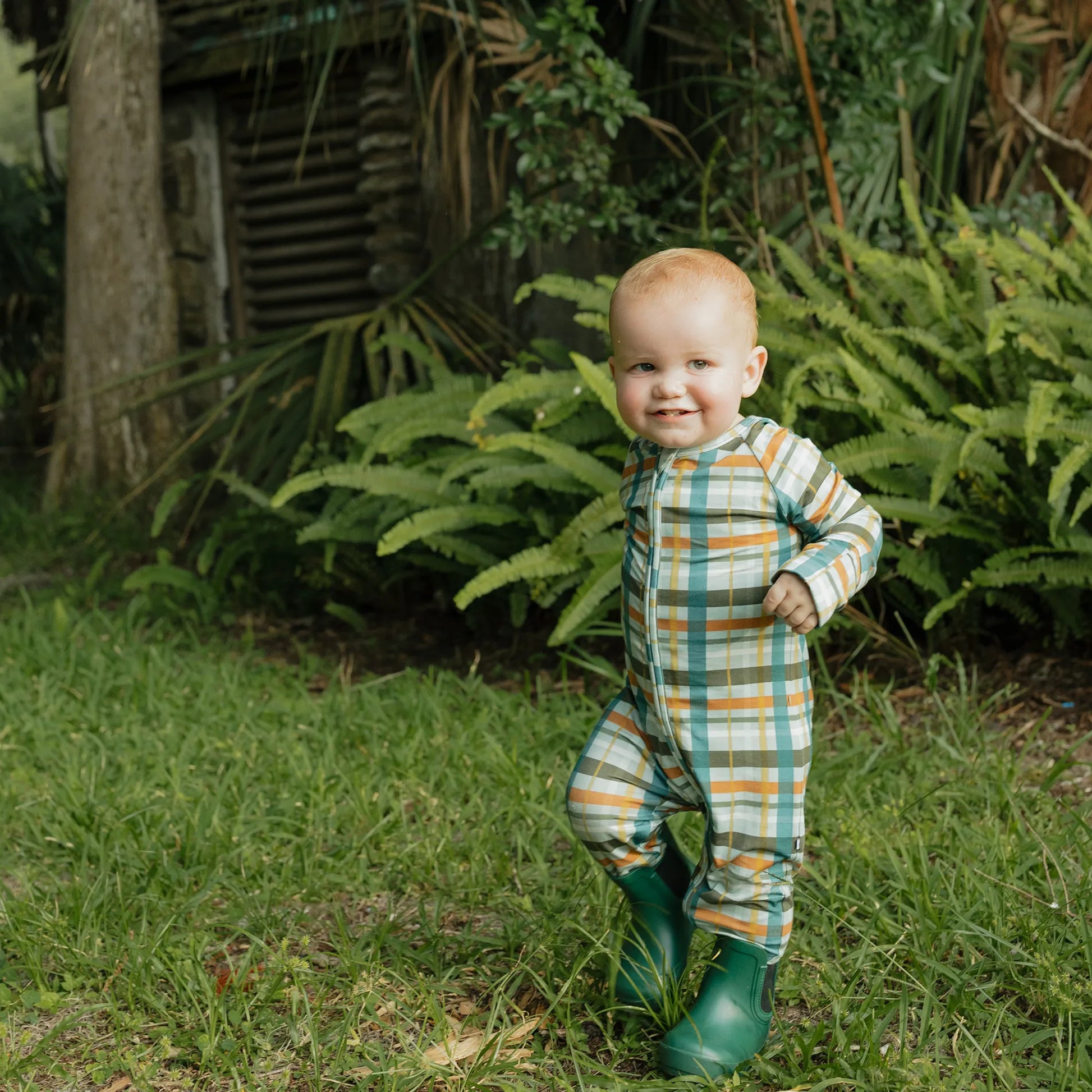 baby wearing fall color plaid zippie on greenery background. 