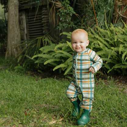 baby wearing fall color plaid zippie on greenery background. 