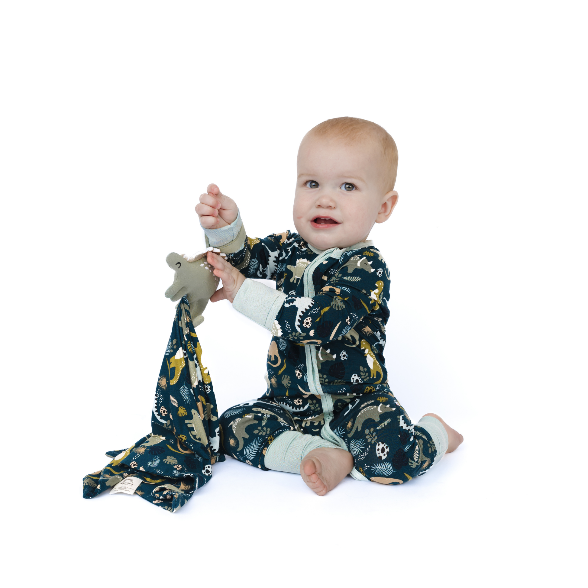 Baby in a patterned outfit holding a matching blanket and toy on a white background