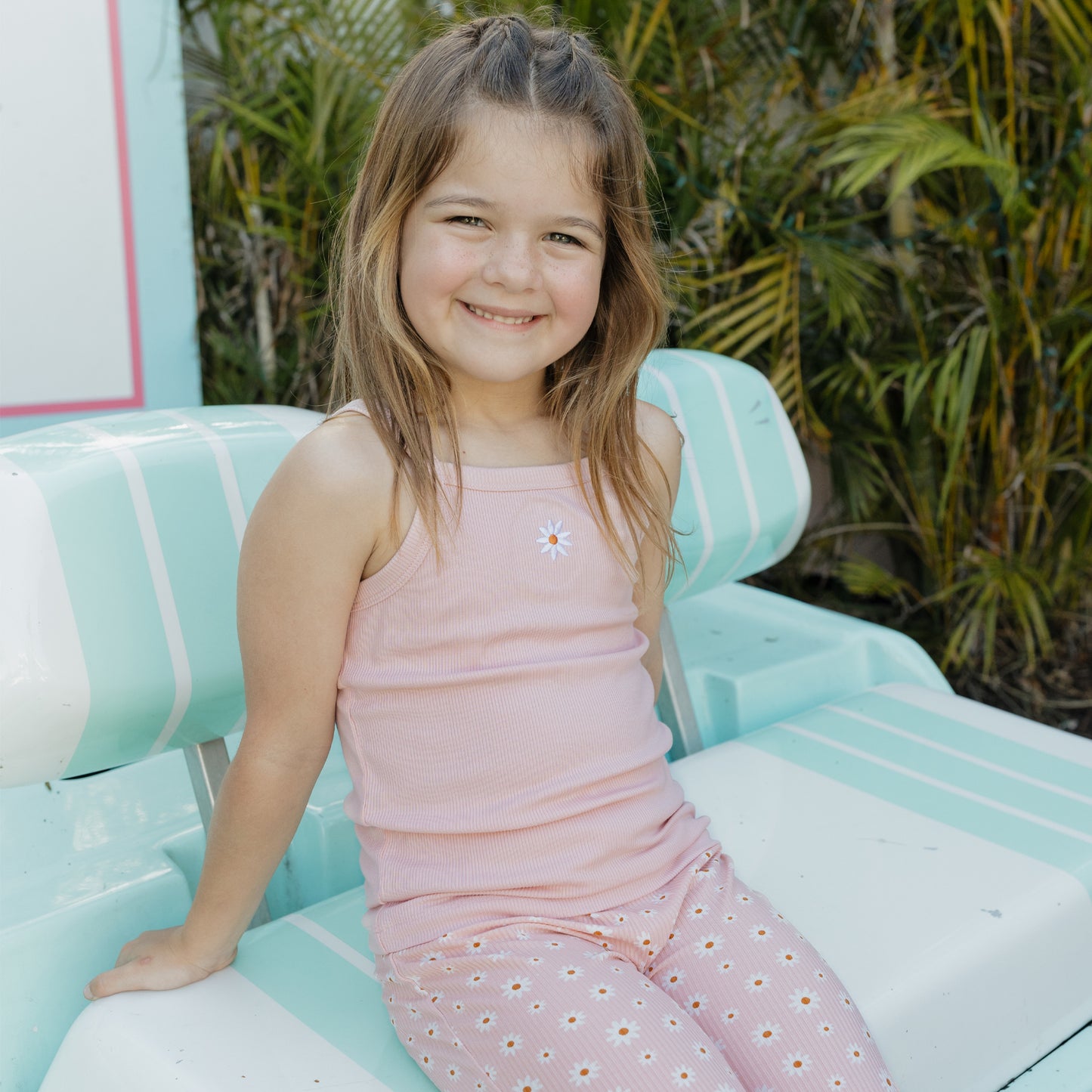 Young girl in a pink dress sitting on a blue car with greenery in the background