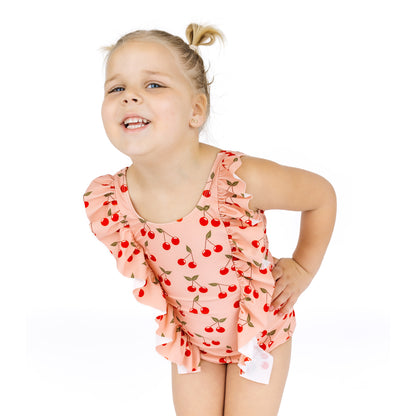 Young girl wearing a pink peach-colored swimsuit with cherry pattern on a white background