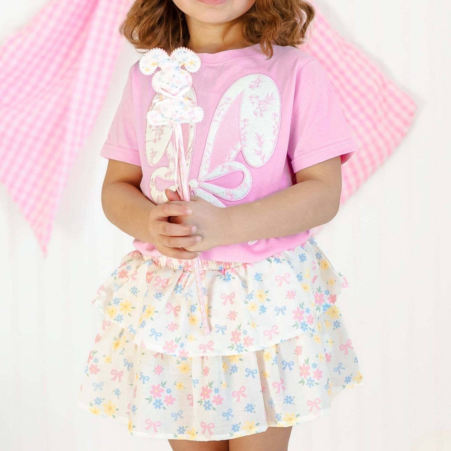 Child wearing a pink shirt with a white design and a floral skirt against a pink background