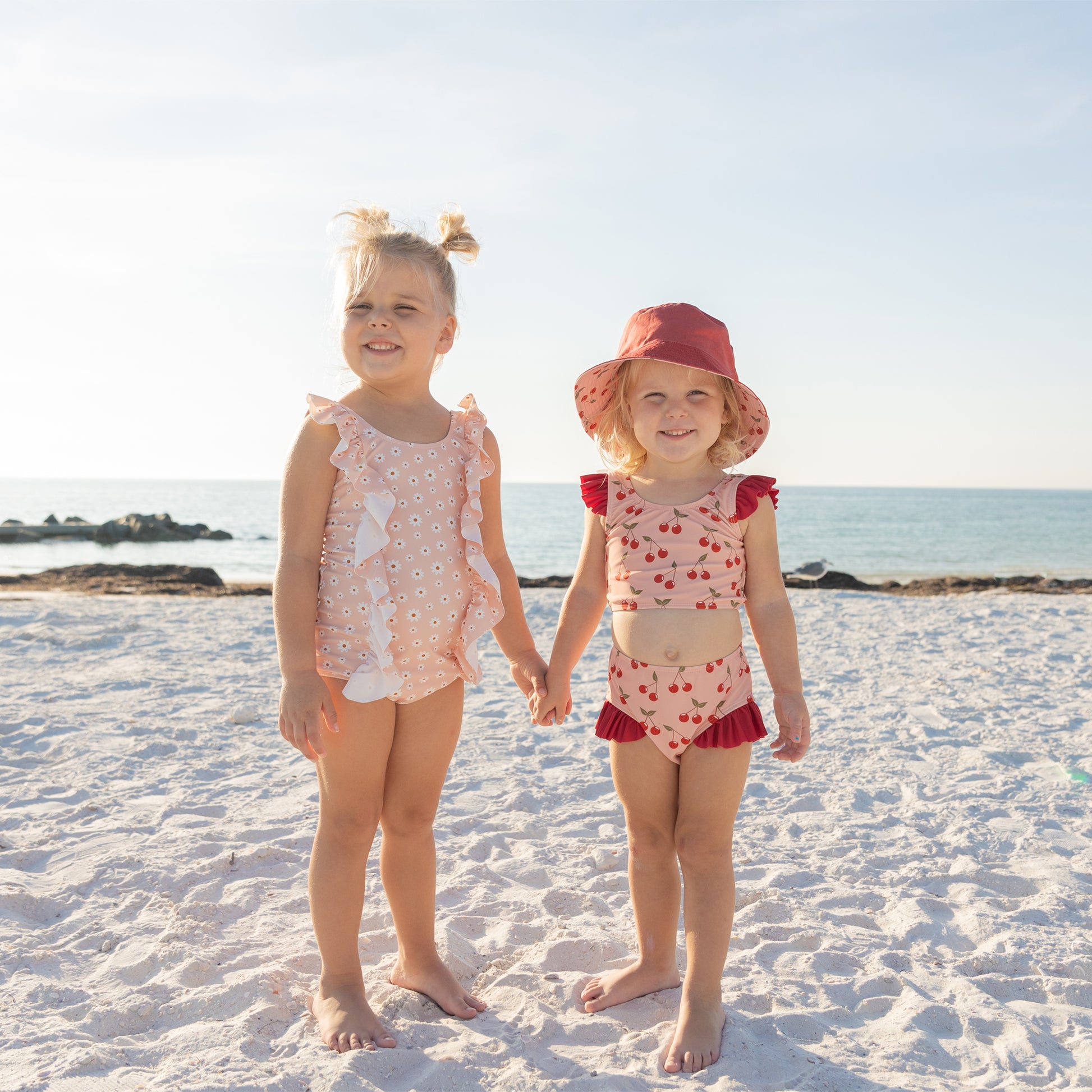 Two young girls in matching swimsuits standing on a sandy beach.