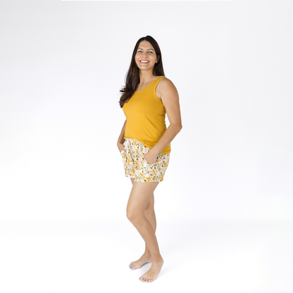 Woman wearing a yellow tank top and floral bee shorts on a white background