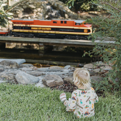Child in All Aboard the Dinosaur Train™ bamboo convertible pajamas watching a toy train outdoors