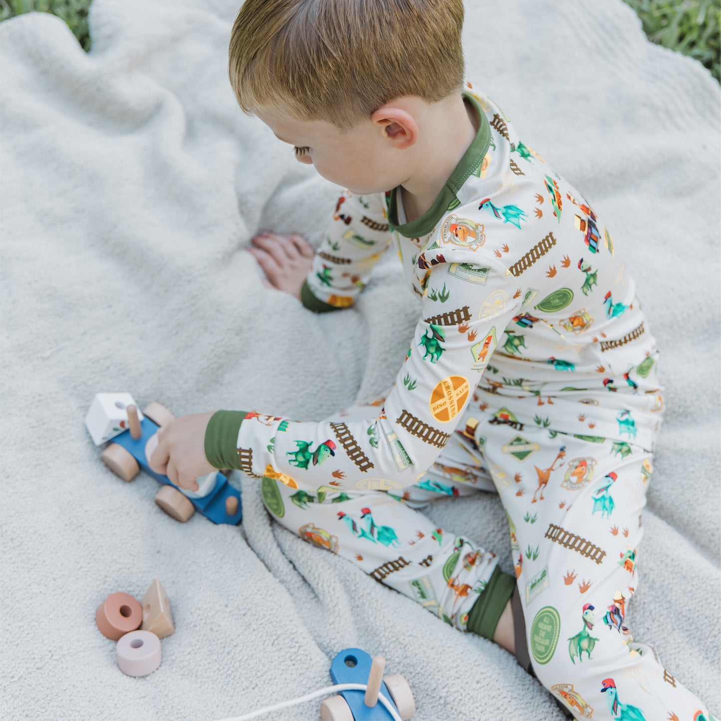 Toddler wearing All Aboard the Dinosaur Train™ bamboo pajamas playing in the blanket. 