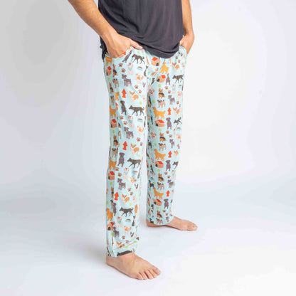 Close up of a man wearing the "dogs bark" relaxed pants. the "dogs bark" print is a mix of various types of dogs, dog houses, dog bones, paw prints, dog food, and tennis balls scattered around a light blue background.