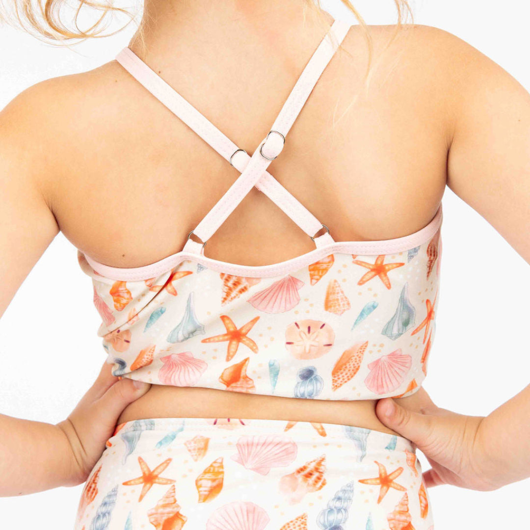 Close up of the cross in the back of the top for our 2 piece Sandy Seashell swimwear. The print reflects seashells is different peach, pink and blue colors. The trim on the top is light pink. 