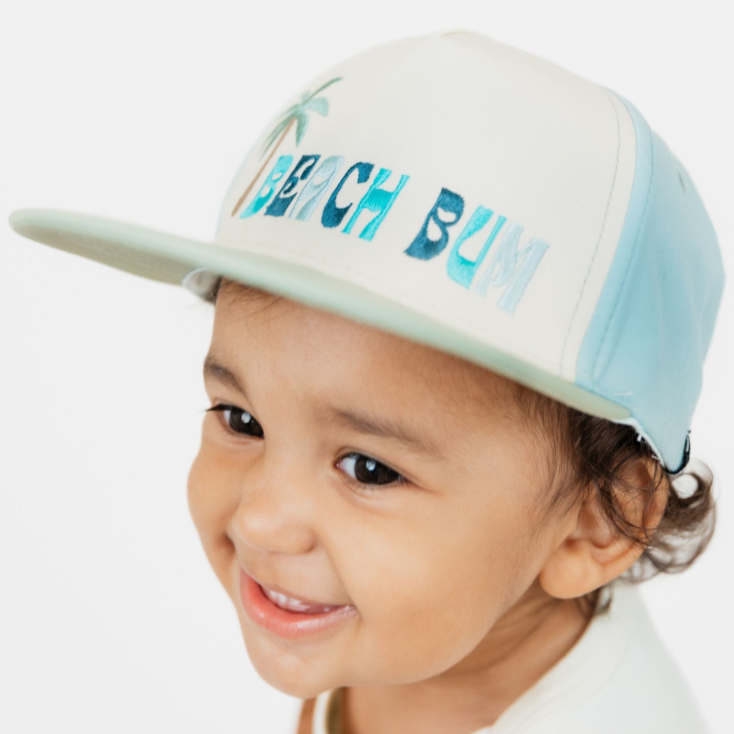 Child wearing a cap with 'Beach Bum' text on a white background
