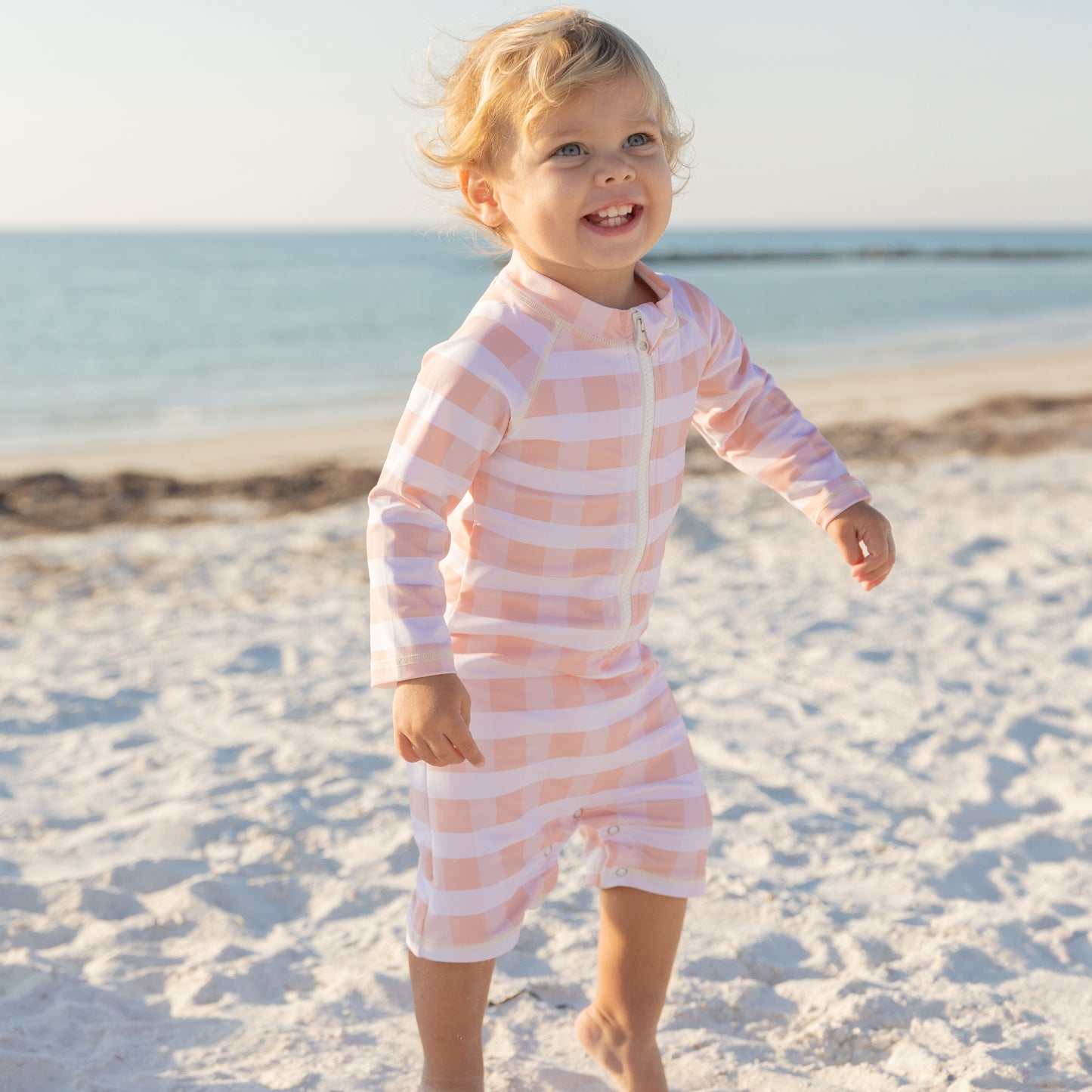 Child in a pink and white striped swimsuit on a sandy beach
