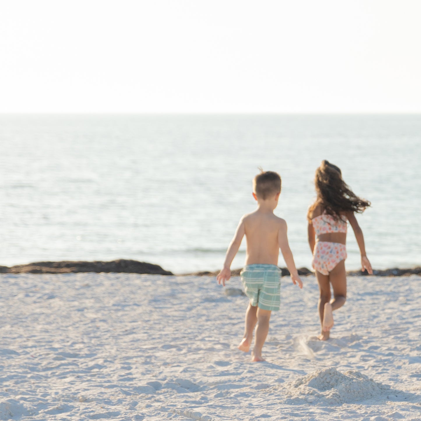 Two children walking on a sandy beach with ocean in the background