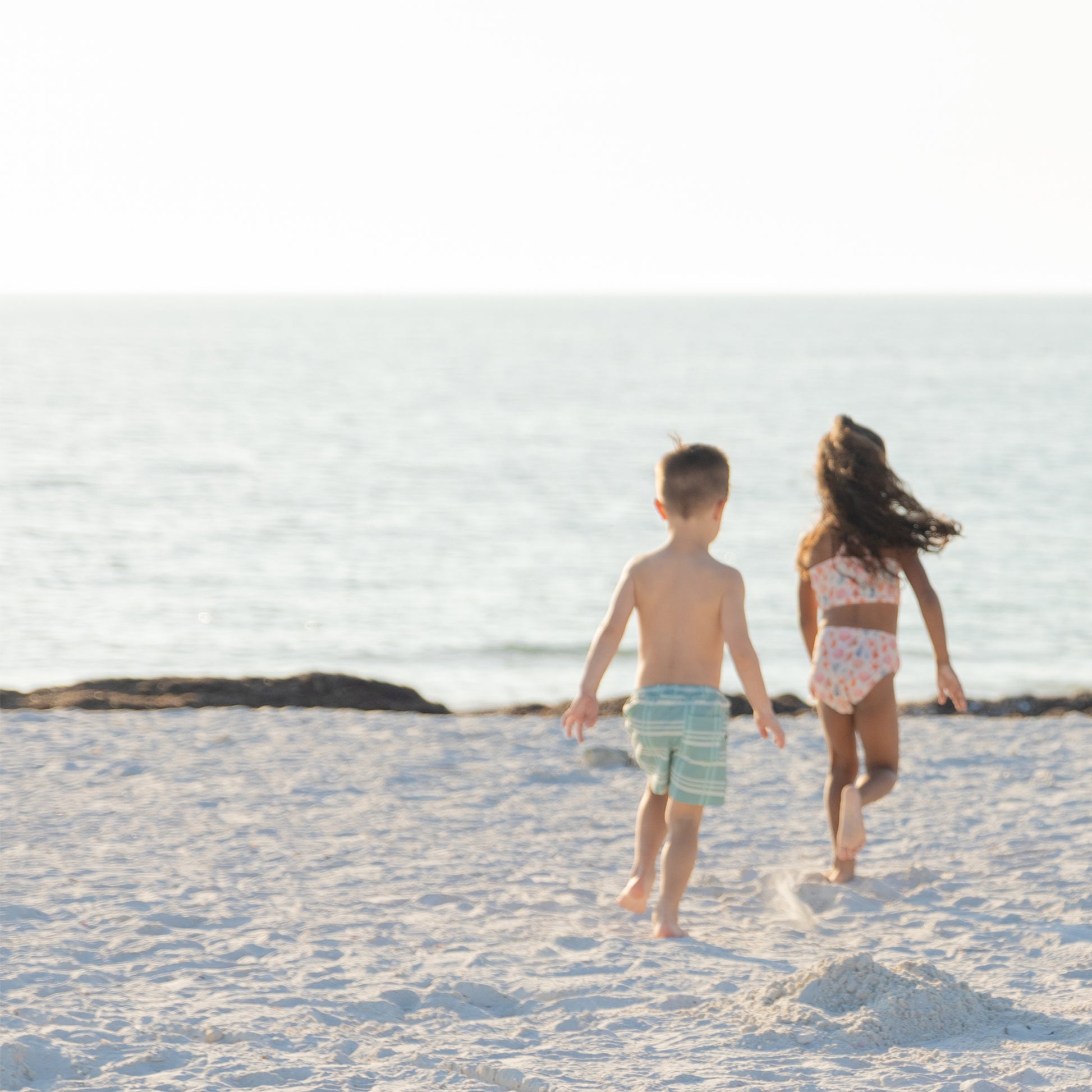 Two children walking on a sandy beach with ocean in the background