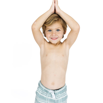 Young boy with striped swim shorts standing against a white background