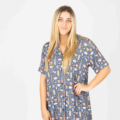 A woman wearing a short-sleeved multicolor nightgown with a geometric pattern, buttoned at the top, standing against a neutral background.
