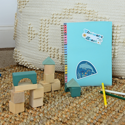 a notebook leans up against a pillow. the blue notebook has the clearwater sticker on it  .