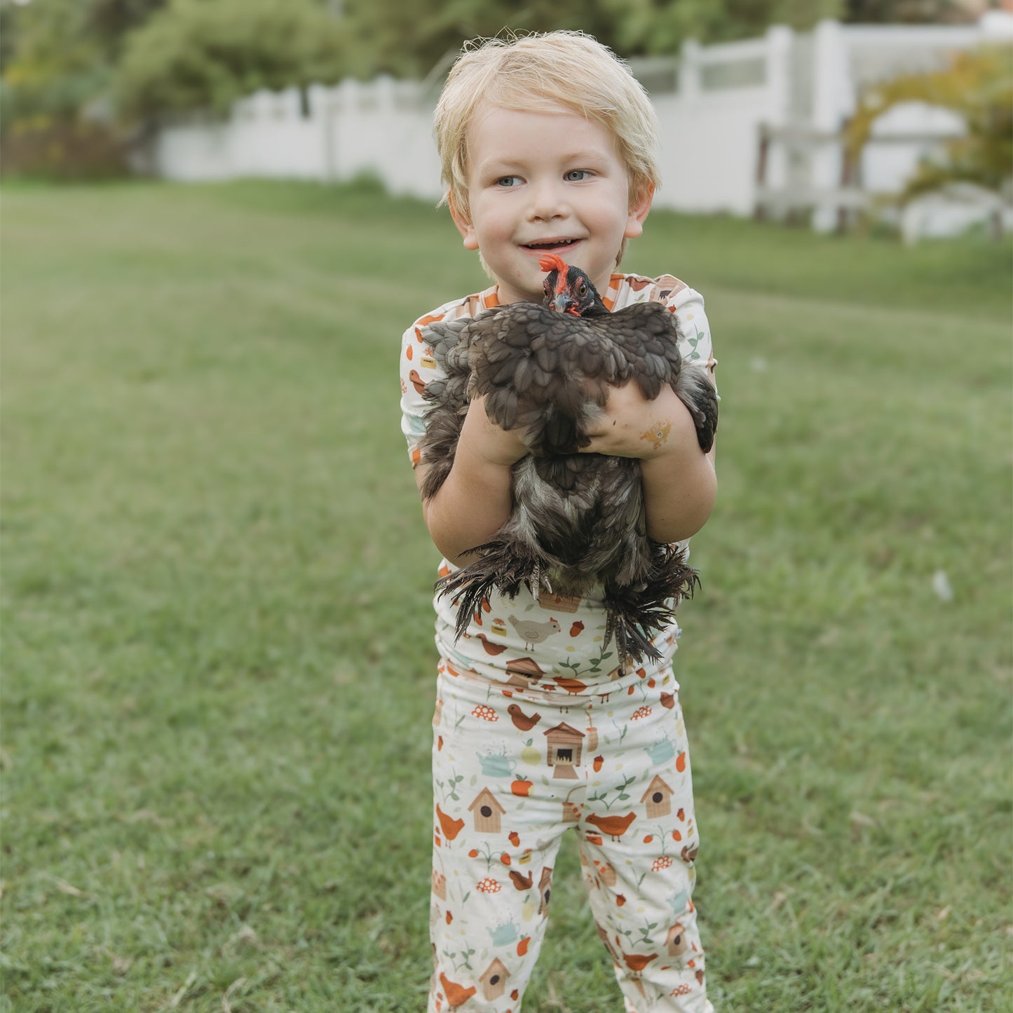 Smiling child holding a chicken while wearing Cozy Cottage bamboo kids pajama set.