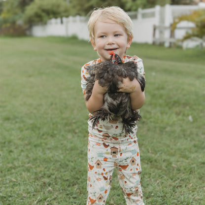 Smiling child holding a chicken while wearing Cozy Cottage bamboo kids pajama set.