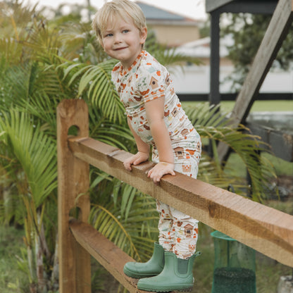 Child wearing Cozy Cottage bamboo kids pajamas climbing a farm fence, breathable short sleeve set.