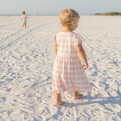 Little girl walking on the beach in a breathable pink gingham bamboo dress designed for spring and summer.