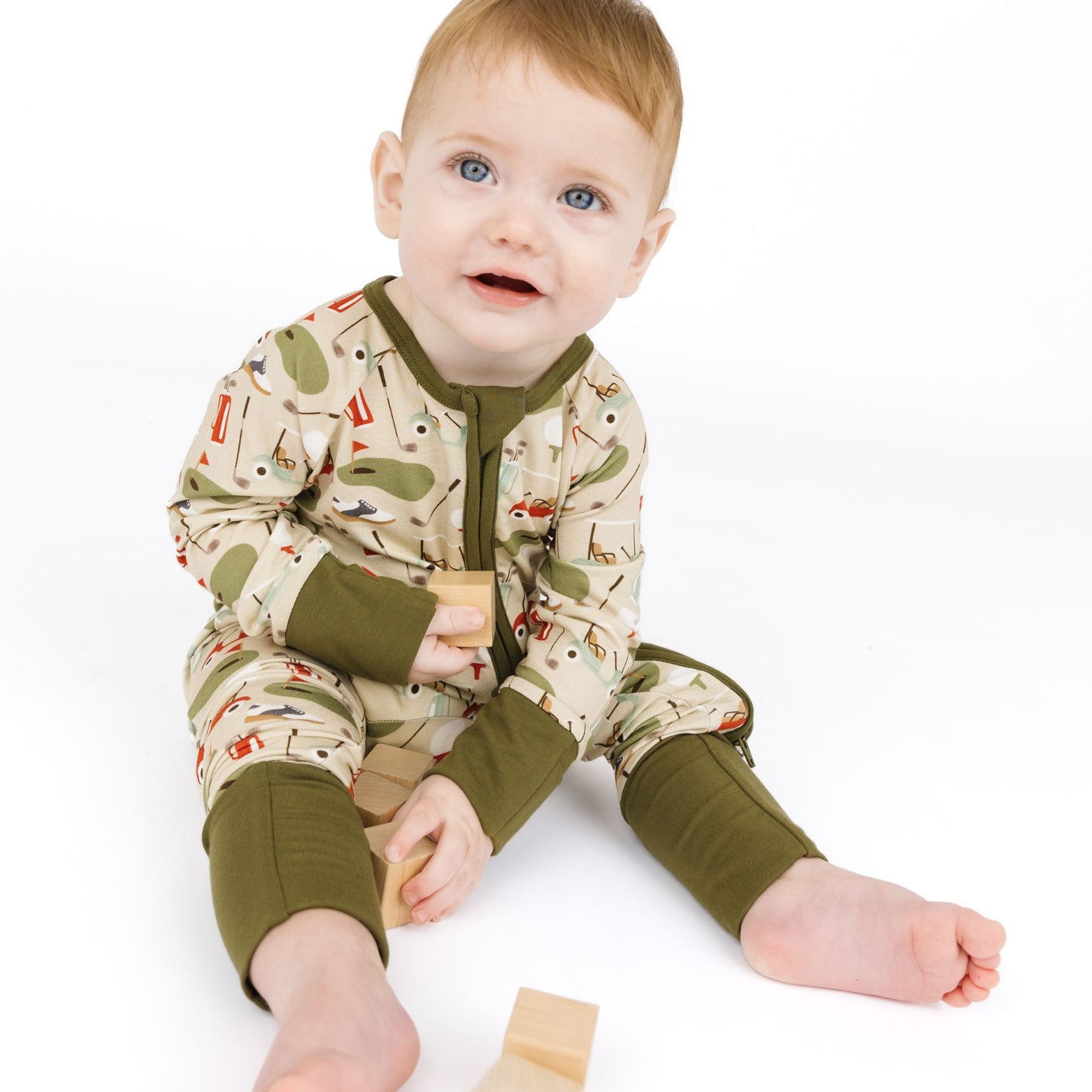 Baby wearing a patterned onesie with green sleeves and legs on a white background
