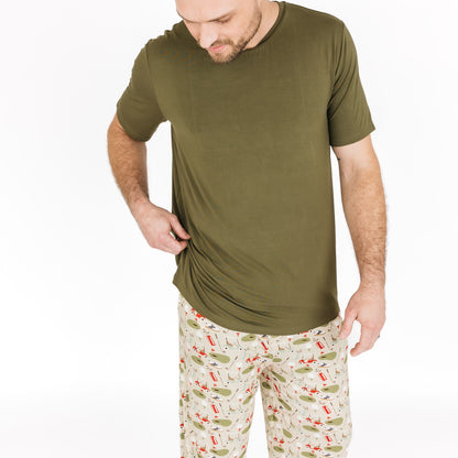 Man wearing an olive green t-shirt and patterned pants on a white background