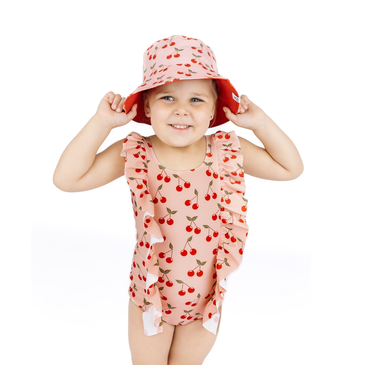 Child wearing a cherry-patterned swimsuit and hat on a white background