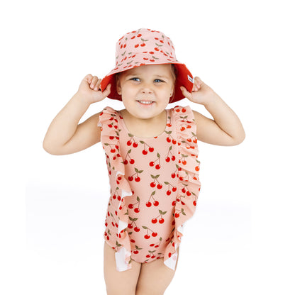 Child wearing a cherry-patterned swimsuit and hat on a white background