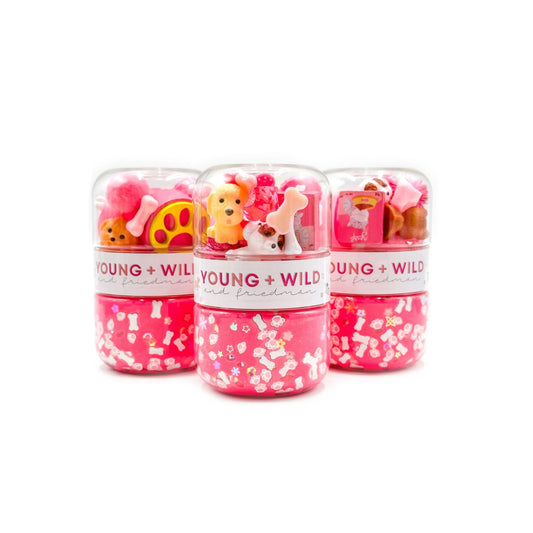 Three clear plastic pet travel capsules filled with pink pet-friendly treats and small toy bones, shown on a white background. The capsules have white labels with pink text reading 'YOUNG + WILD' and 'pet friendly'.