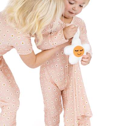 Child in pink floral pajamas holding a plush toy with a face on a white background