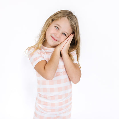 Young girl in a striped shirt posing with hands on face against a white background