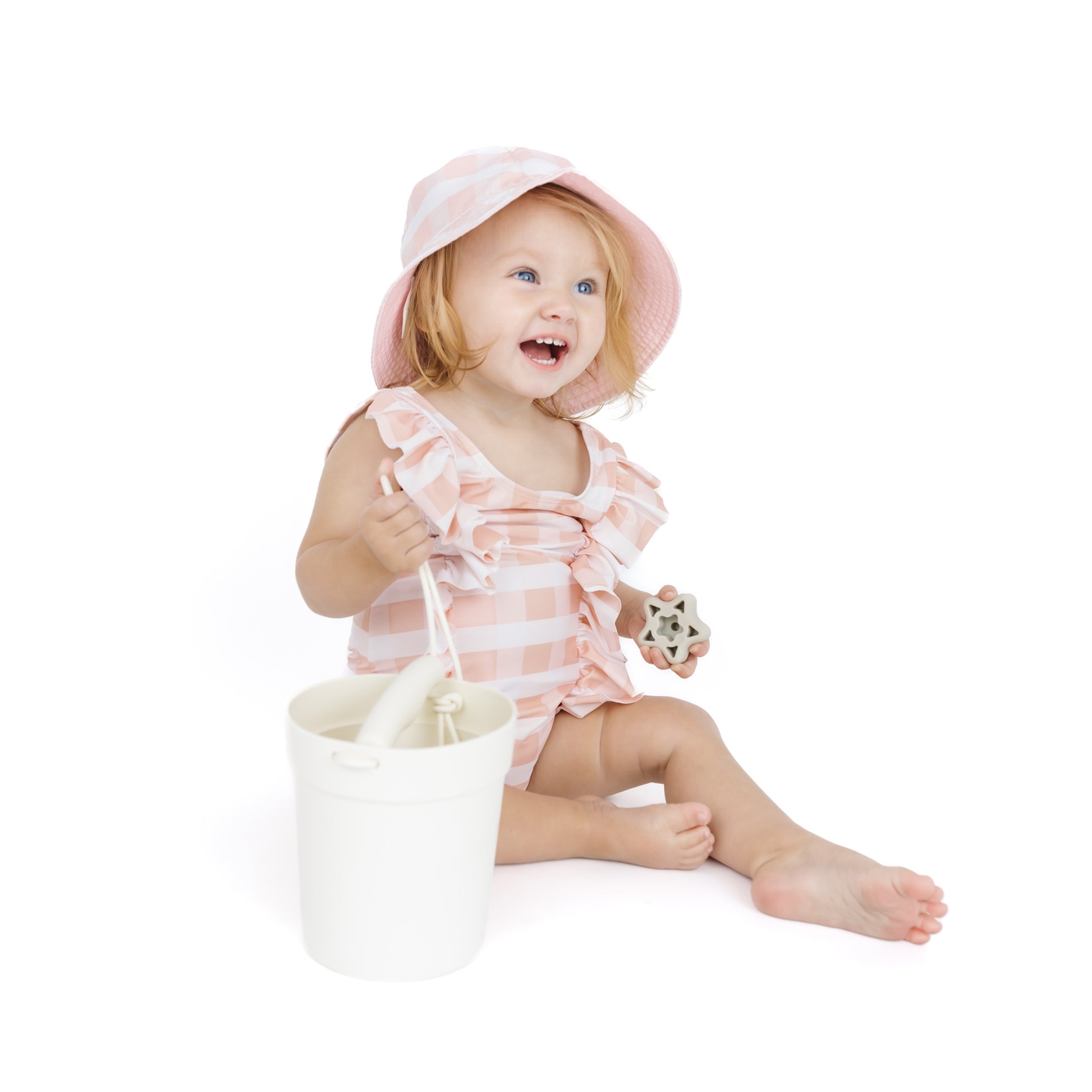 Child in a pink and white striped swimsuit with a matching hat, sitting on a white surface.