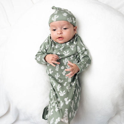 infant baby lays on a white pillow. the baby is in the "stay sharp" gown and hat set. 
