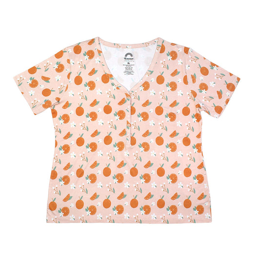 the "freshly squeezed" women's top. the "freshly squeezed" print has an assortment of full and half cut oranges scattered around. there is also flower heads and flower stems that intermingle within the print. this is all space out around a pink background space. 