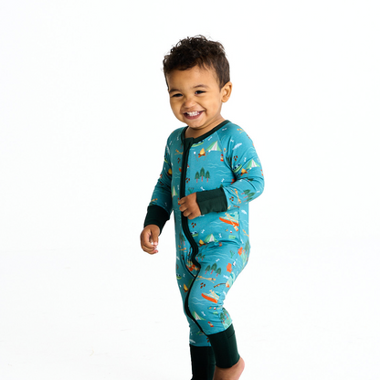 toddler boy is captured walking and laughing. he wears the "jump in the lake" convertible. the "jump in the lake" pattern is a print to capture the day in the life on a lake. you can fine fishing poles, tents, camp fires, adirondack chairs, marsh mellows, ores, canoes, forest trees, and different types of fish and fishing gear.