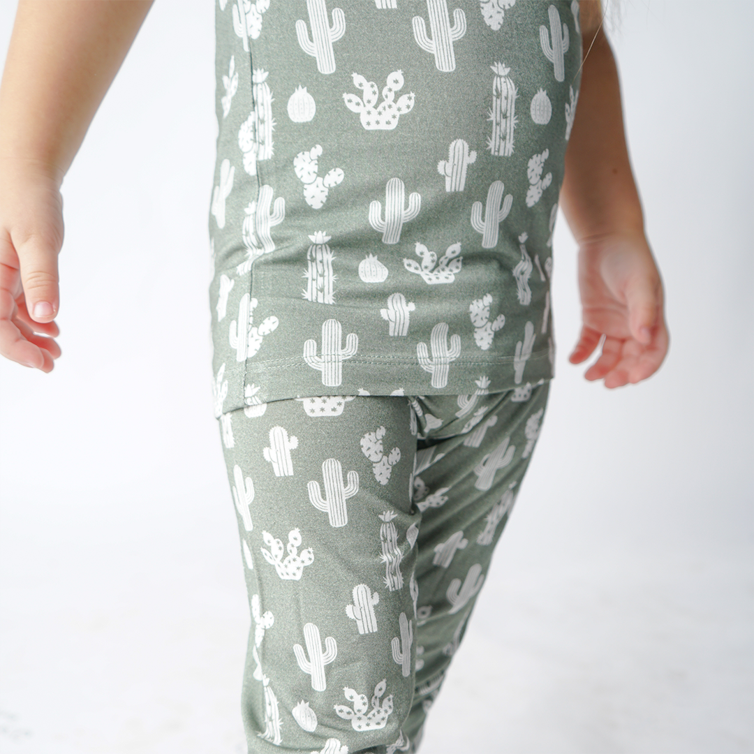 close up and zoomed in photo of a child wearing the "stay sharp" matching pajama set. the "stay sharp" print is a variety of different white cacti on a greyish/green background. 