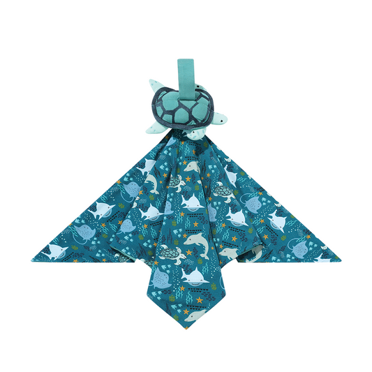 the "ocean friends lovey" is a blanket with the "ocean friends" print and a turtle perched on the top of it. the "ocean friends" print is a combination of dolphins, stingrays, fish, starfish, coral, bubbles, and sharks, all spread out on a deep sea blue background. 
