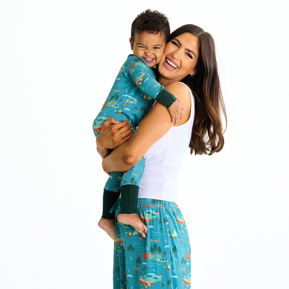 mom smiles and laughs into the camera she hugs her toddler boy. their faces are cutely smooshed together. the toddler wears the "jump in the lake" convertible. the mom wears the "jump in the lake" relaxed pants. the "jump in the lake" pattern is a print to capture the day in the life on a lake. you can fine fishing poles, tents, camp fires, adirondack chairs, marsh mellows, ores, canoes, forest trees, and different types of fish and fishing gear.