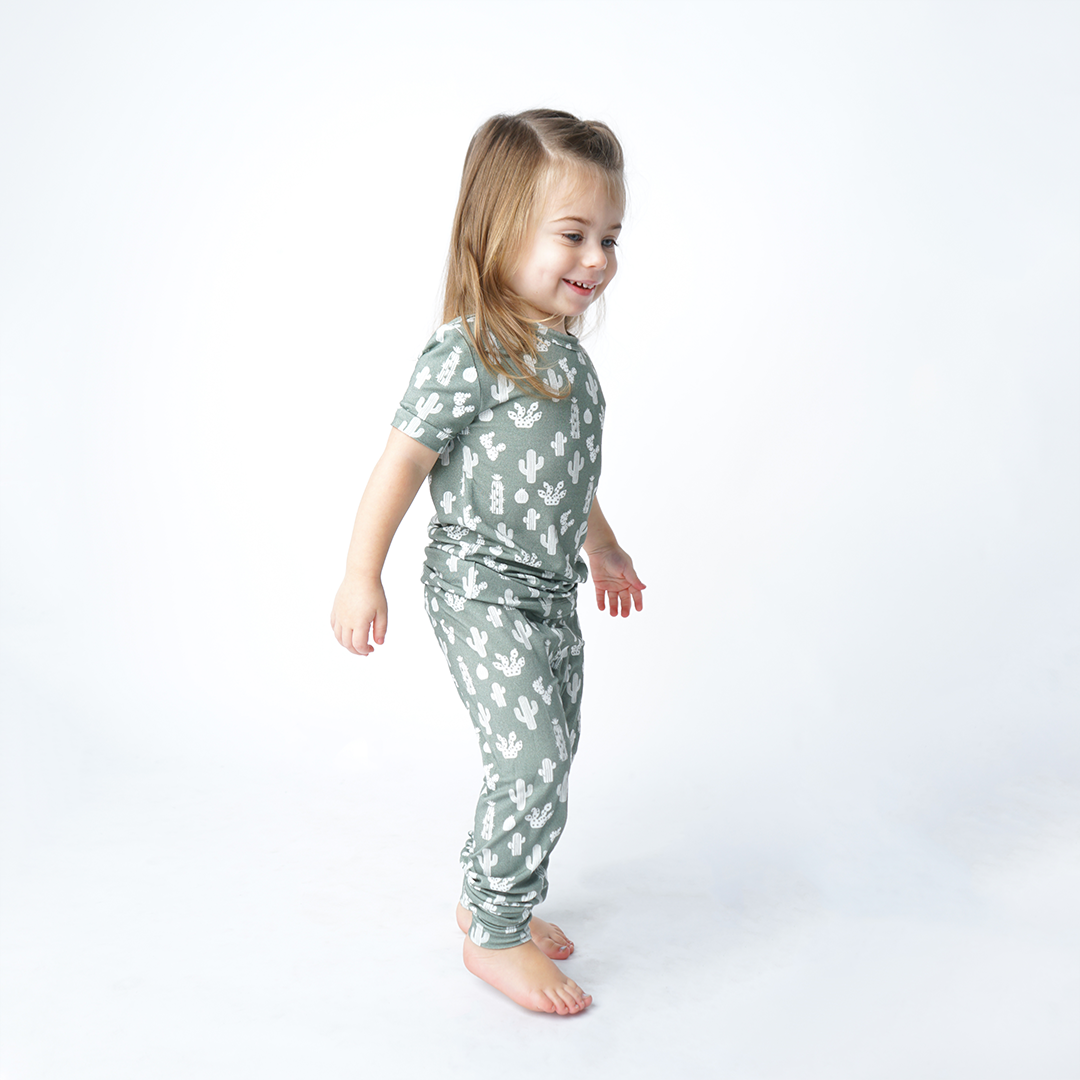 little girl plays and walks around in her "stay sharp" matching pajama set. the "stay sharp" print is a variety of different white cacti on a greyish/green background. 