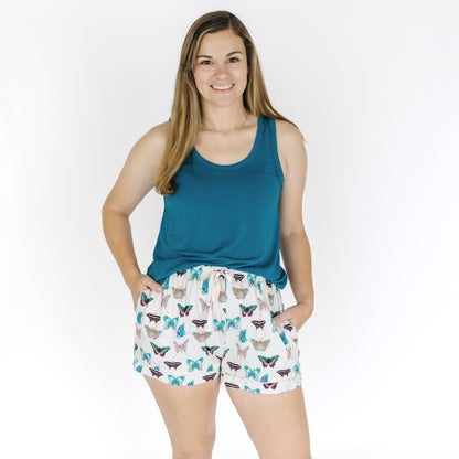 Woman wearing a teal tank top and patterned shorts on a white background
