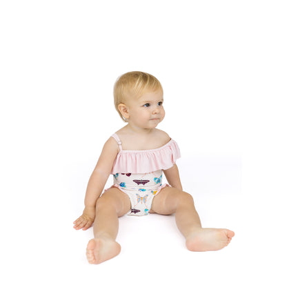 Baby sitting on a white background wearing a pink top and patterned diaper.