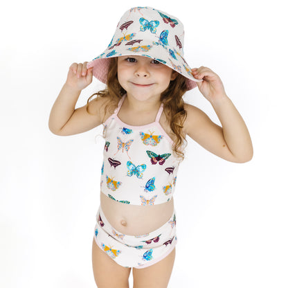 Child wearing a butterfly-patterned swimsuit and hat on a white background