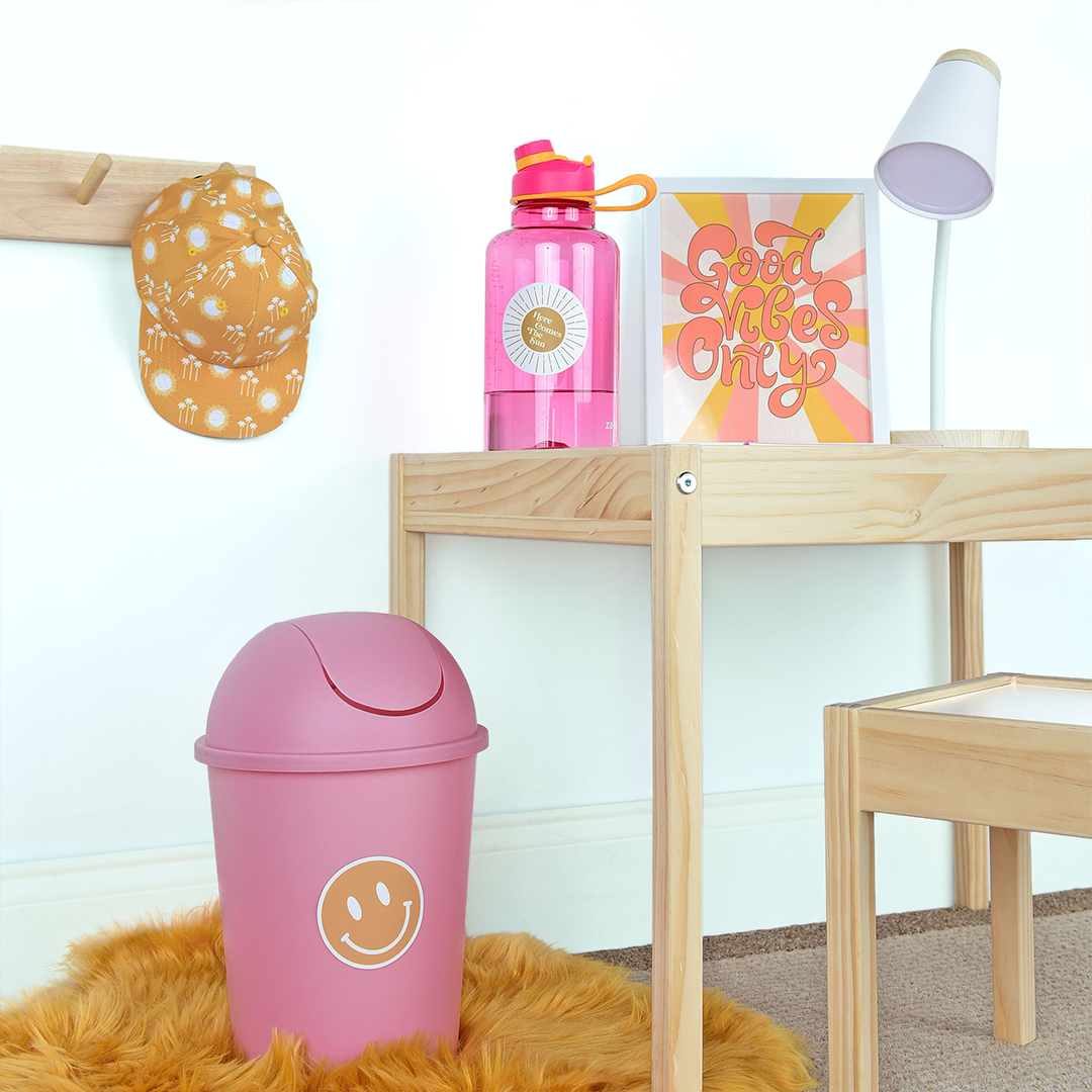the yellow happy face sticker is placed on a trash can next to a cute desk. 